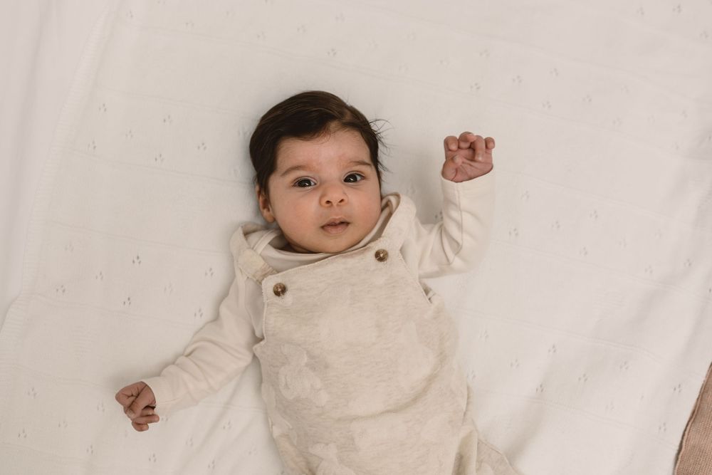 Baby wearing a cozy white knit outfit lies on soft white bedding.