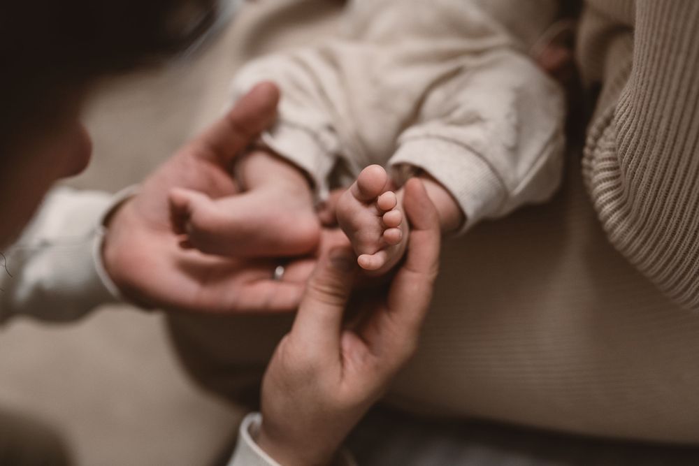 Close up of hands holding a newborn baby's tiny feet with soft focus and warm lighting.