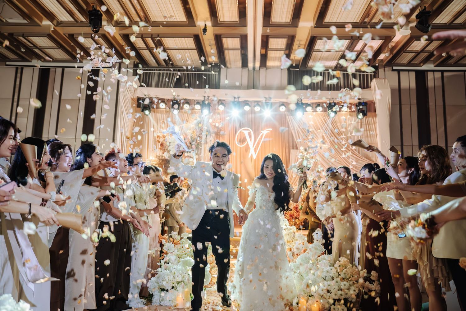 Bride and groom walking through confetti shower at elegant wedding reception with glowing backdrop.