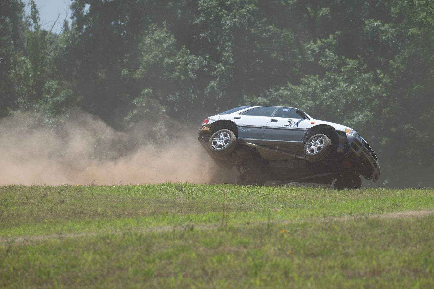 SUV driving on a dirt road creating a cloud of dust in a rural setting.