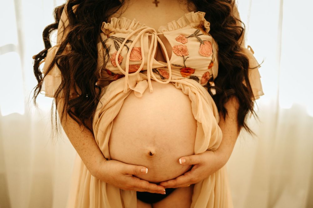 Intimate maternity photo showing pregnant belly in peach-colored dress.