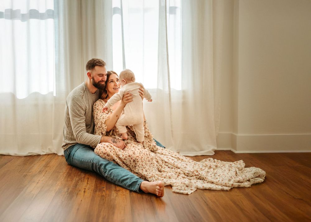 Intimate family moment on hardwood floor with flowing dress and natural lighting.