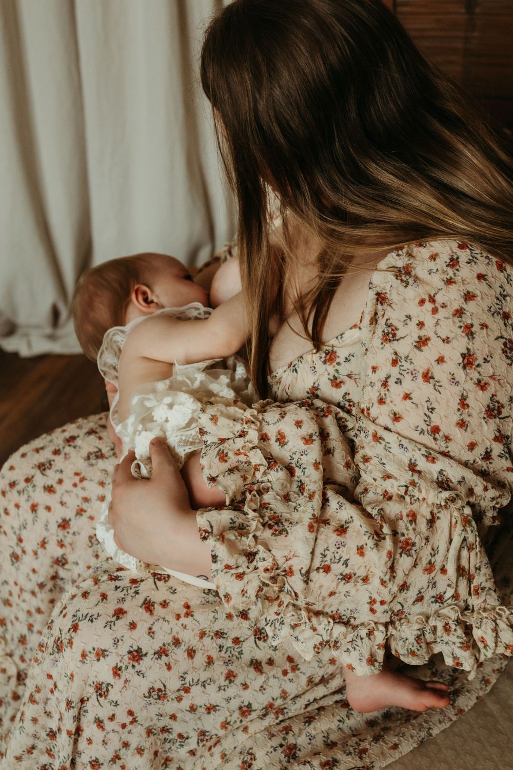 Intimate parenting moment captured in floral dress on wooden floor.