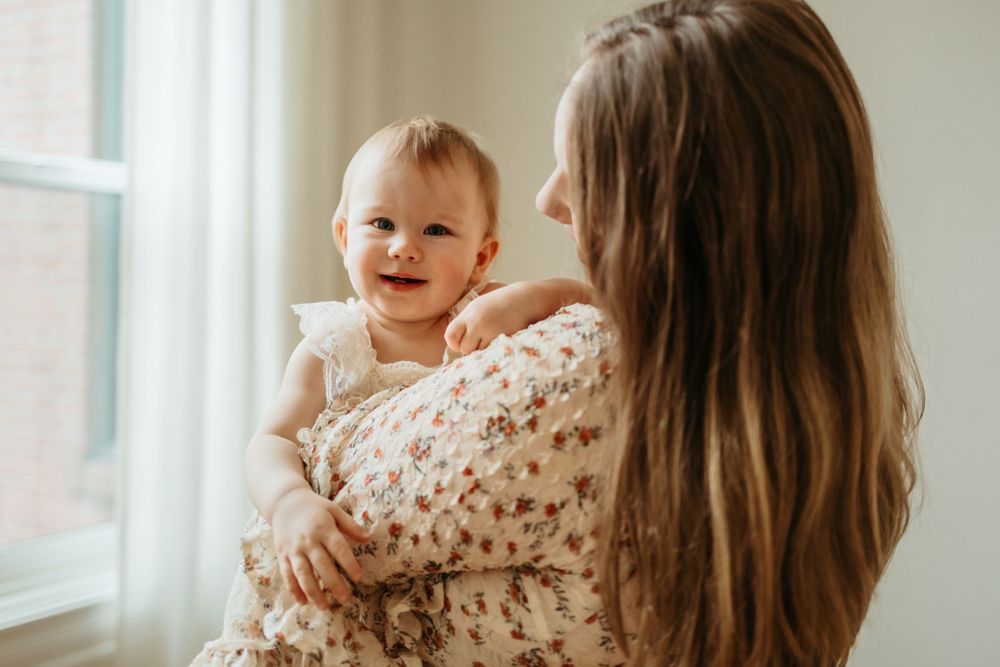 Joyful interaction between parent and child by a sunlit window in matching light-colored outfits.