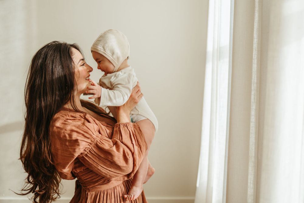 Tender moment between parent and baby in matching rust-colored outfits by window.