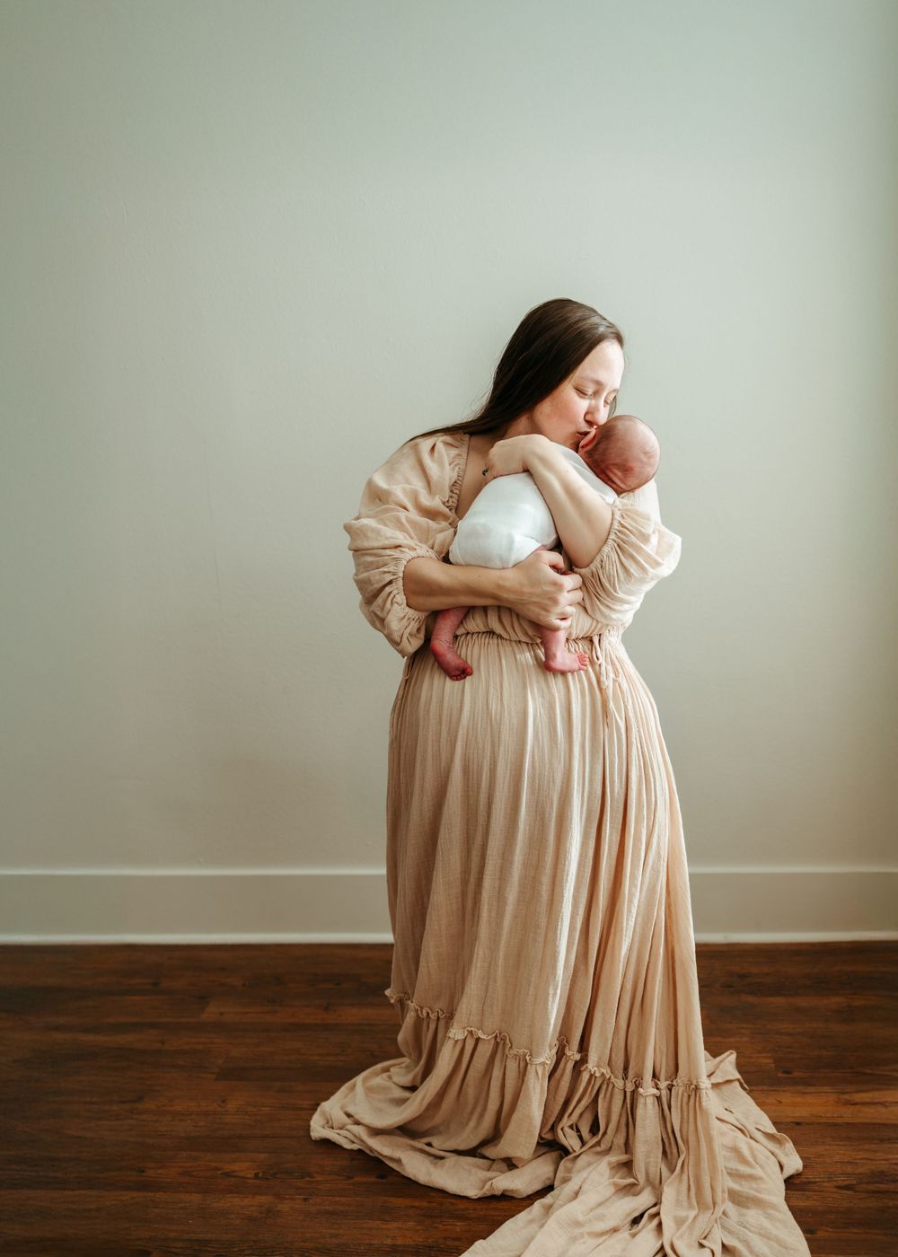 Maternity portrait with flowing beige dress against minimalist backdrop.