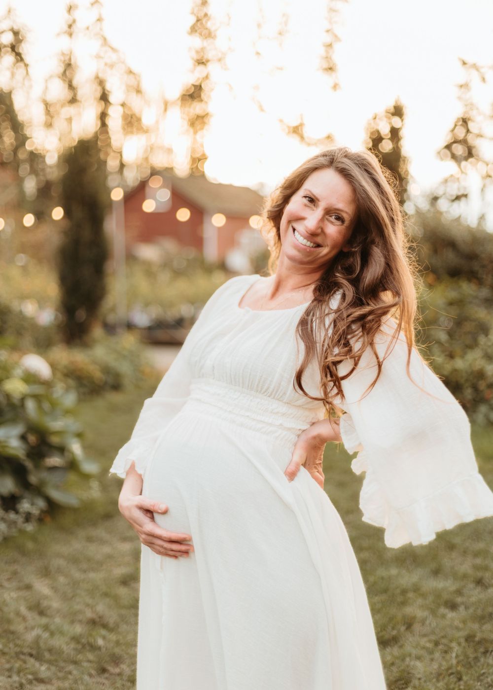 Joyful maternity moment captured in white dress during golden hour outdoors.