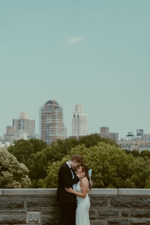 A romantic couple embraces on a rooftop terrace overlooking the Manhattan skyline on a hazy summer afternoon.