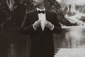 A black and white photo series shows a formal wedding party posing by a serene lake in elegant attire.