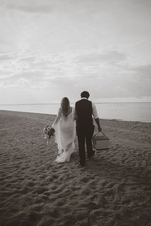 Black and white photo series of newlyweds walking together on a sandy beach with cloudy sky in the background.