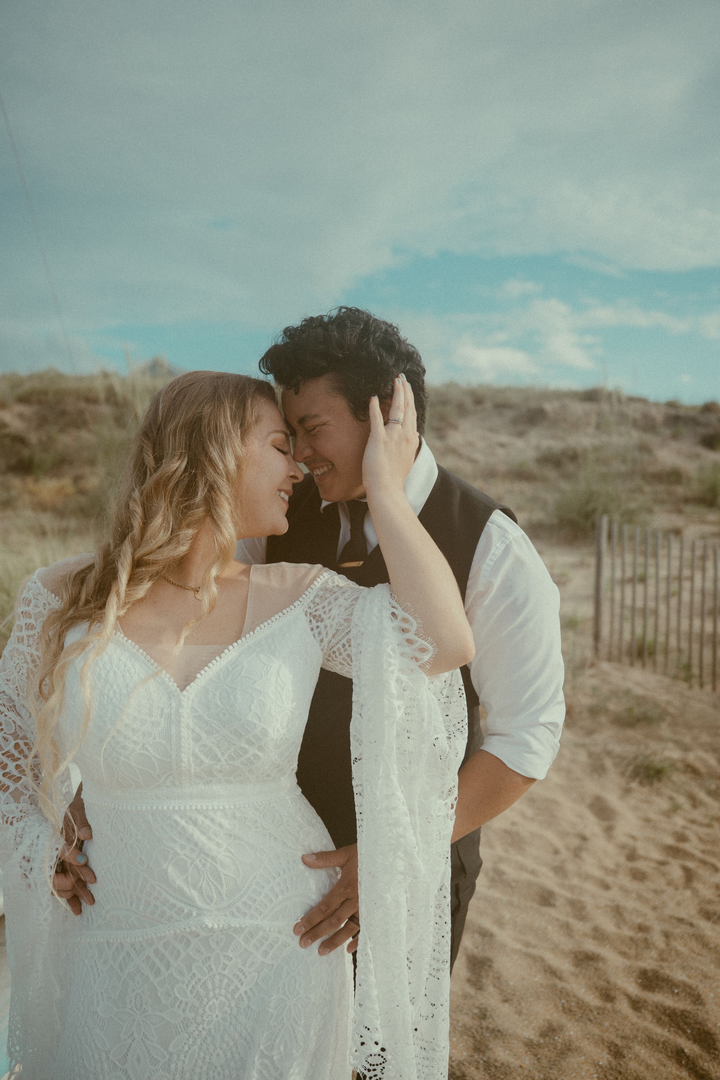 Romantic couple sharing intimate moments on a sandy beach with cloudy skies in the background.