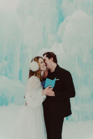 A romantic winter wedding photo series showing a couple embracing against a backdrop of ethereal blue ice formations.