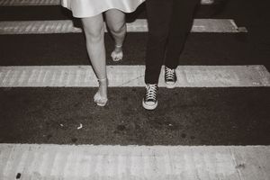Black and white photo showing legs and feet walking across a crosswalk or pedestrian crossing on a city street.