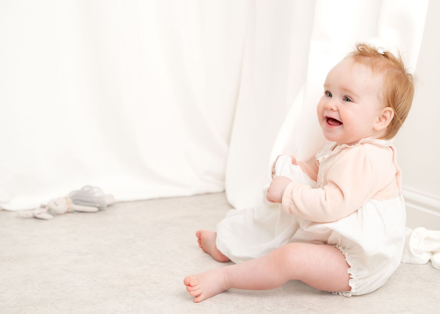 Baby in white outfit crawls and plays during bright studio photoshoot.