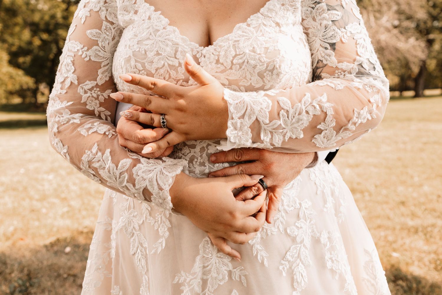 Bride and groom embracing showing wedding rings on lace long sleeve wedding dress.