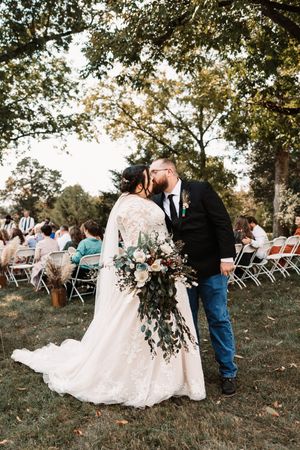 Newlyweds sharing first kiss as married couple during outdoor wedding ceremony recessional.