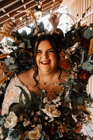 Joyful bride laughing while surrounded by lush floral arrangement with roses and eucalyptus.