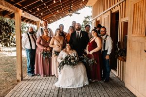 Wedding party posing together on rustic barn porch with bridesmaids in mauve and burgundy.