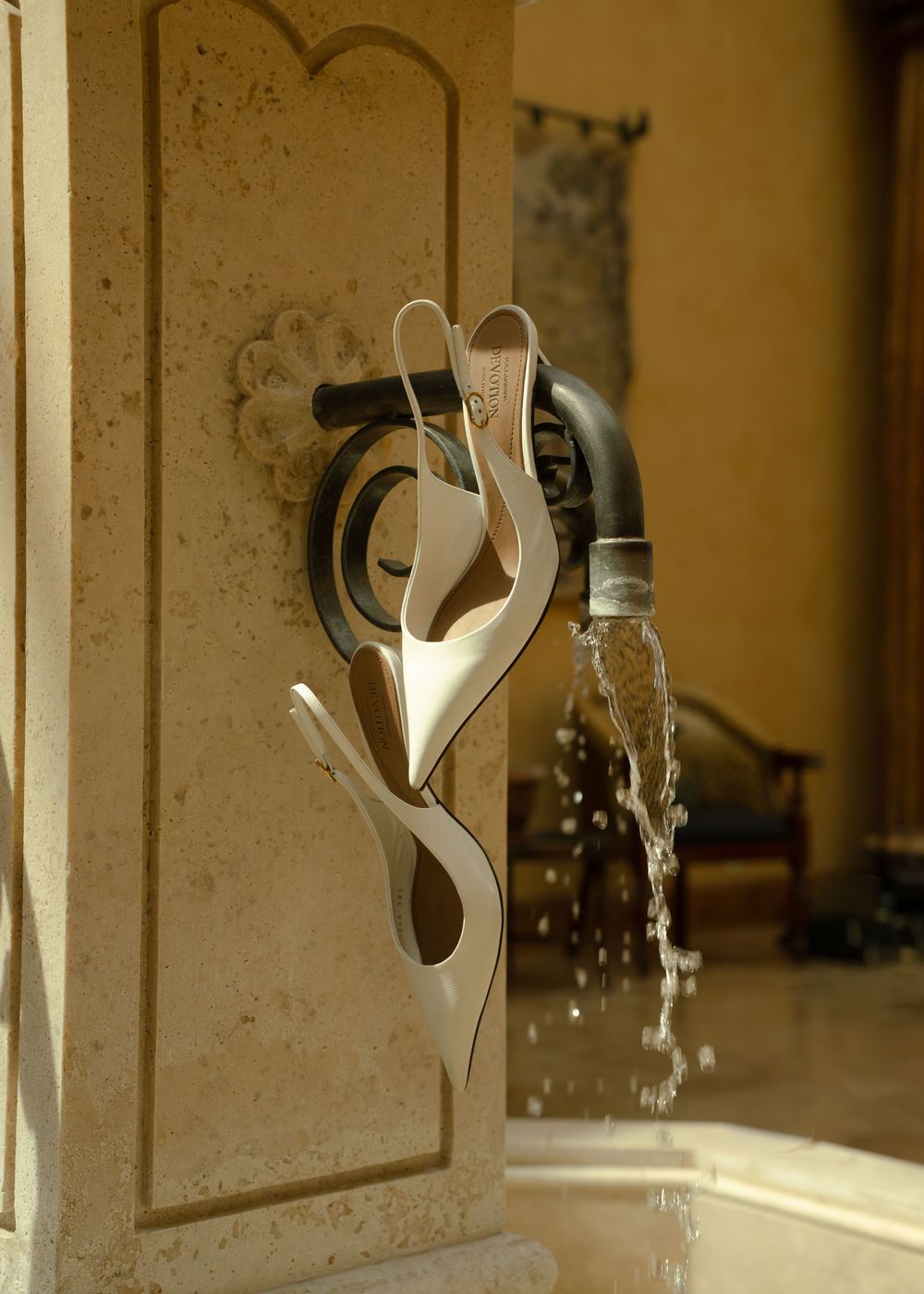 Decorative metal sculpture fountain with flowing water on a stone wall in an elegant outdoor setting.