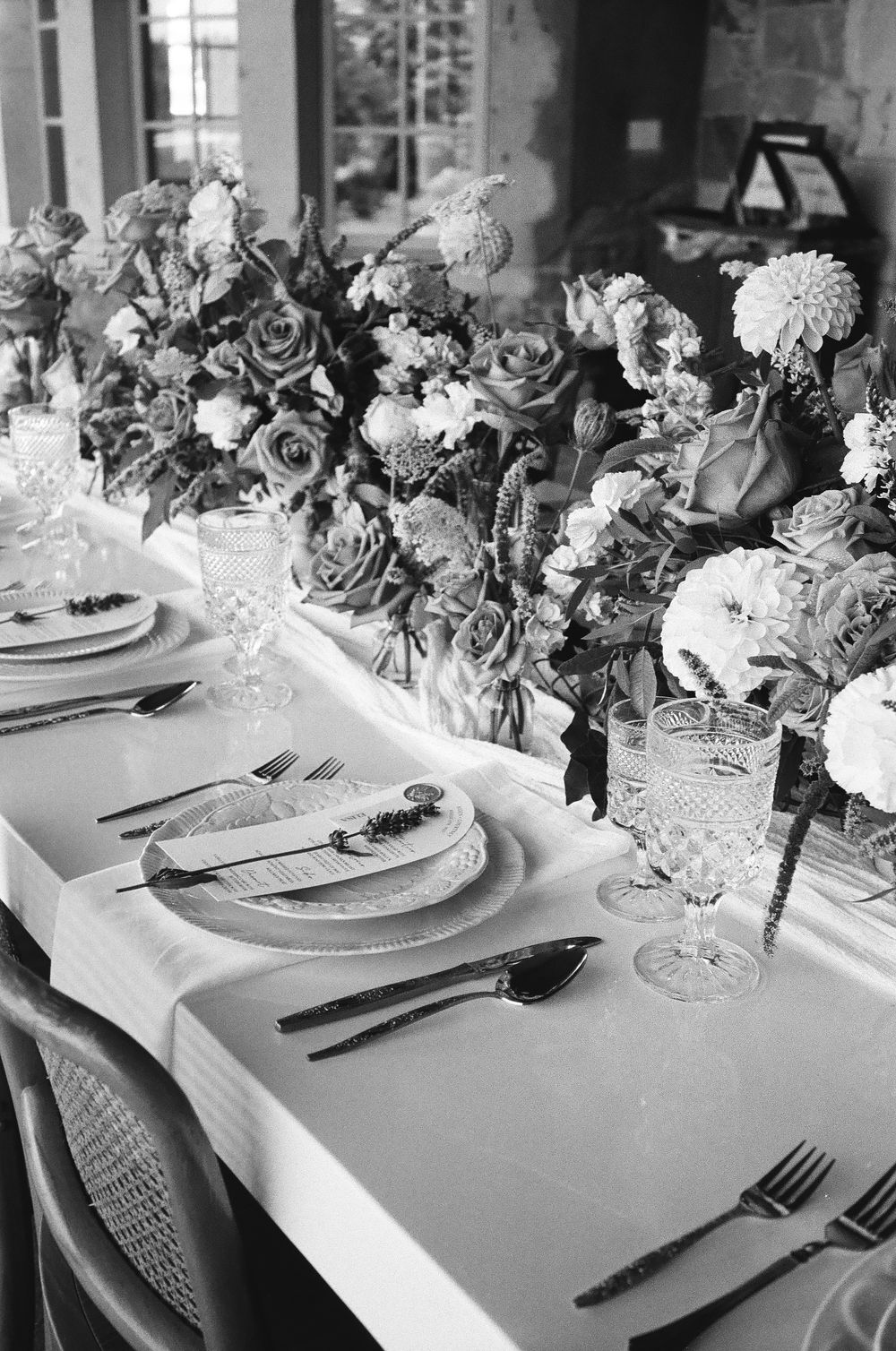 Black and white photo of an elegant wedding table setting with floral centerpieces, crystal glassware, and fine china.