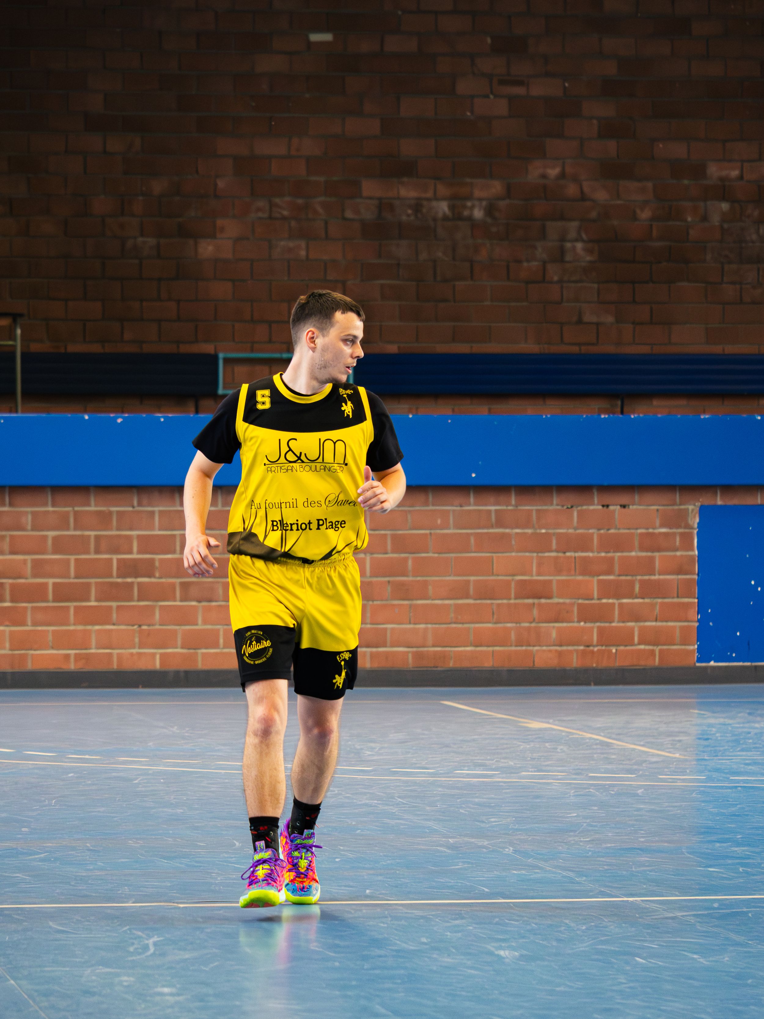 joueur de basket avec couleurs jaune et noir qui court à l'occasion d'un match en intérieur