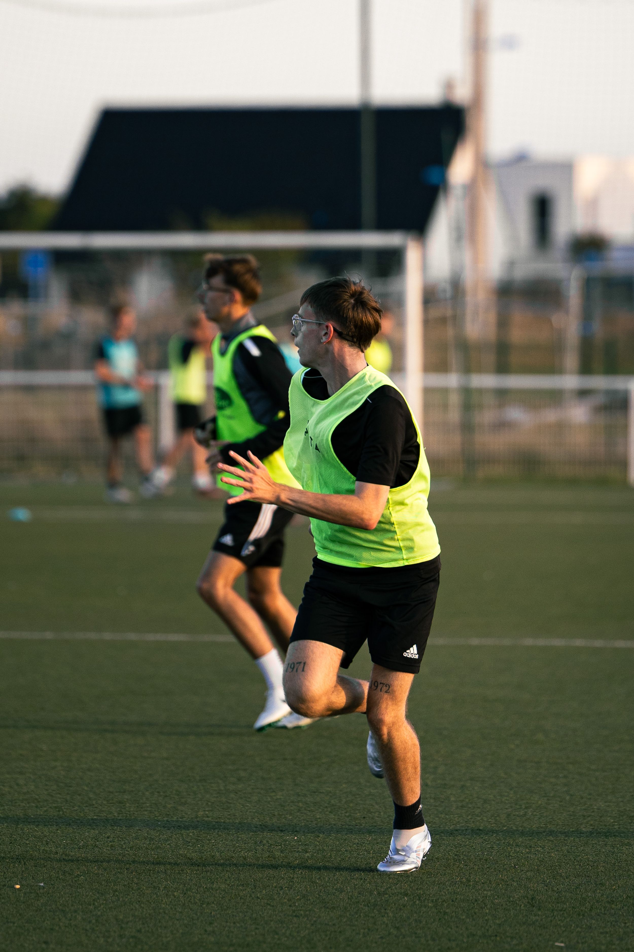 joueur de football avec un t-shirt vert qui court pour réceptionner une passe sur un terrain synthétique vert