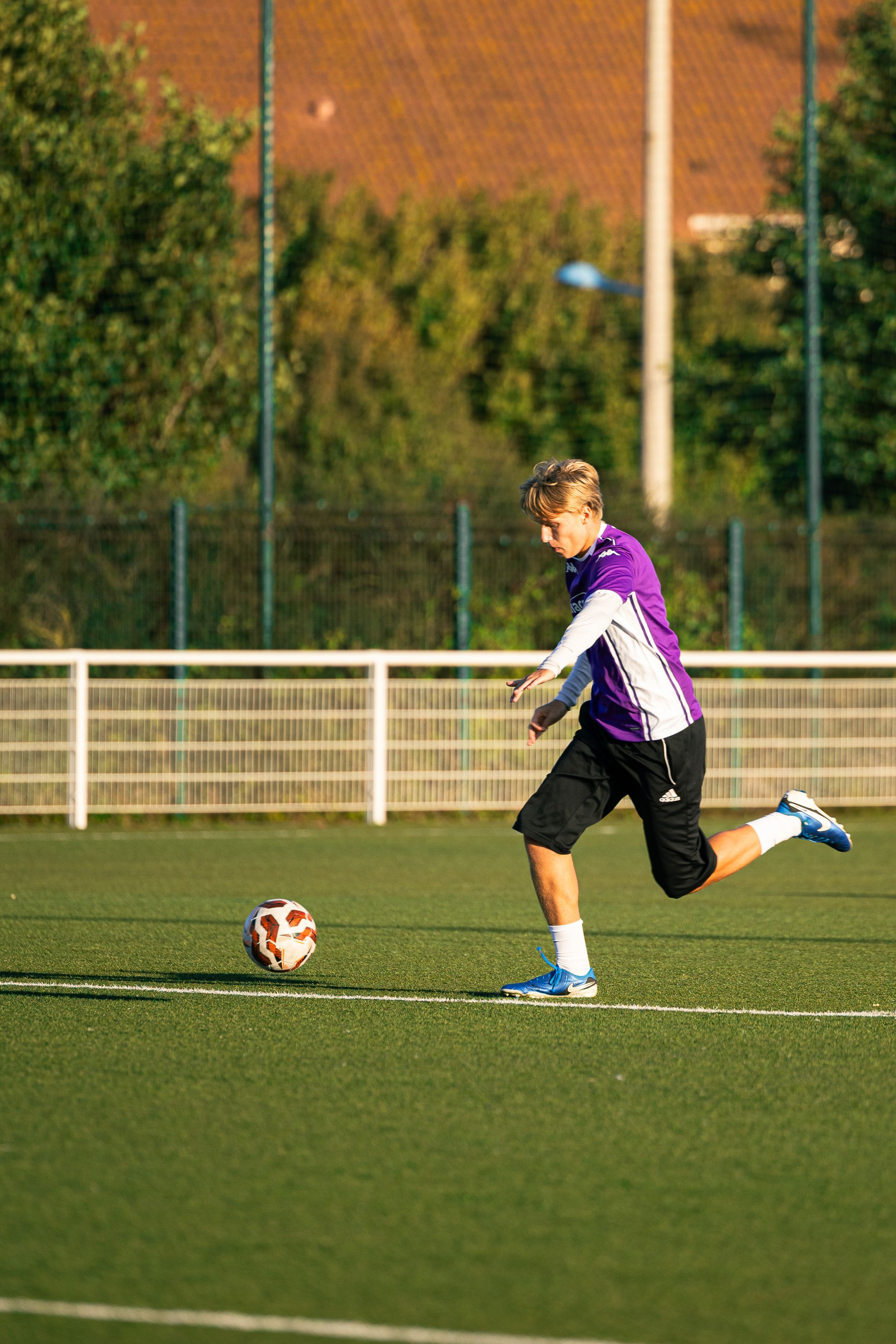 joueur de football avec haut violet qui tire au but