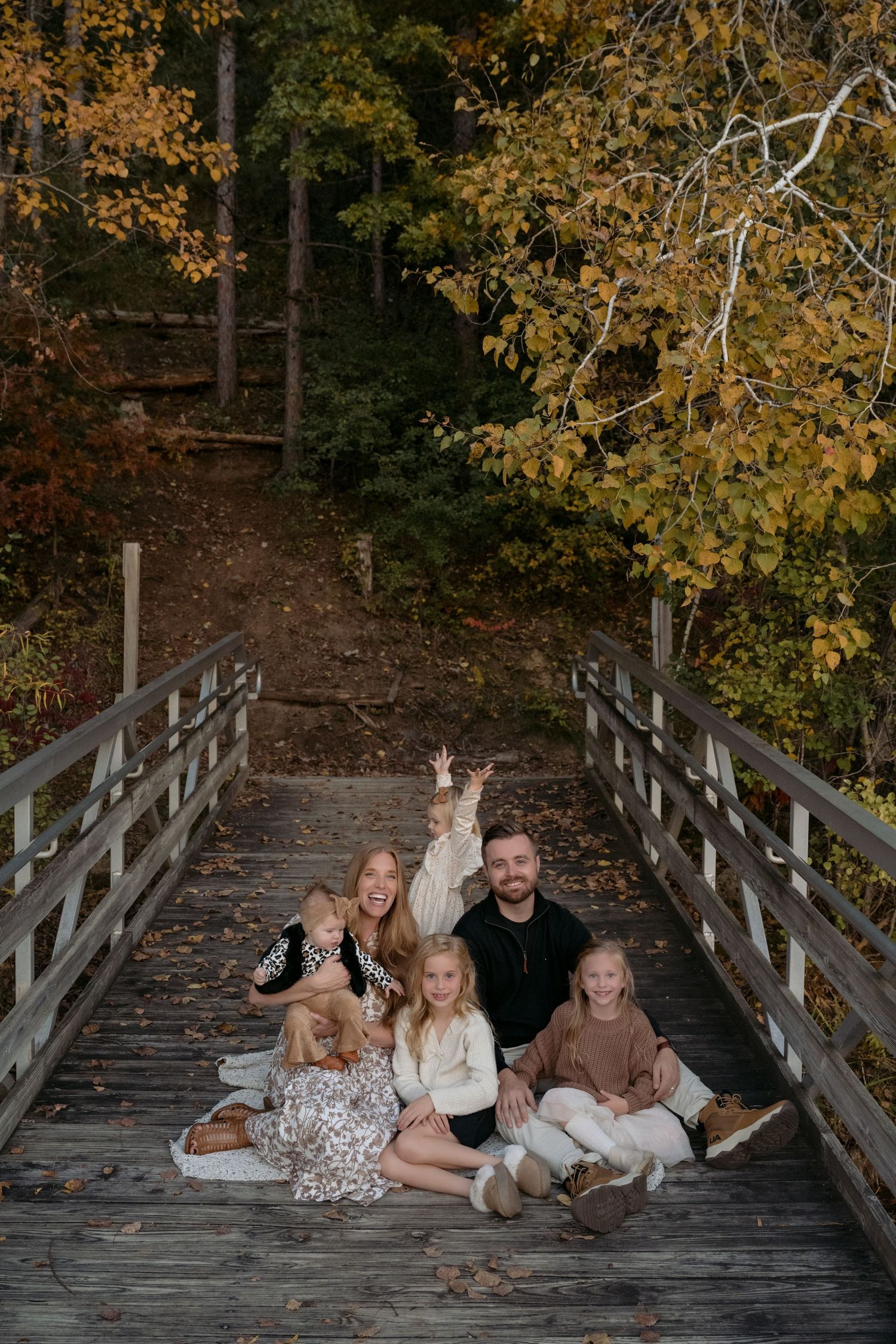 Parents and four young kids sit on a dock during peak fall color for an outdoor lifestyle family session in Hudson, WI.