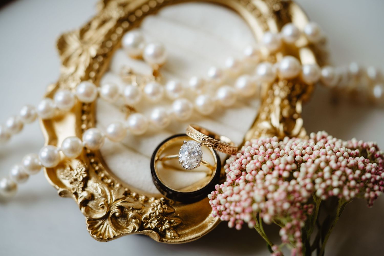 Elegant pearl and gold wedding jewelry details arranged on a textured white surface with rings and bracelet.