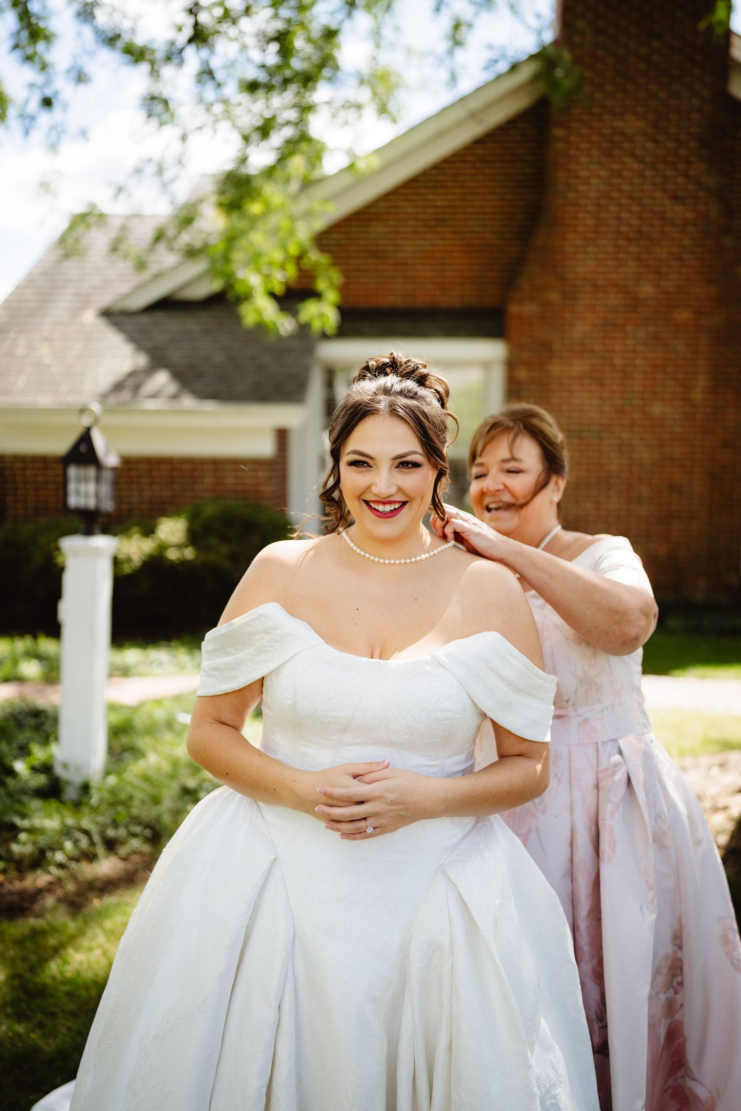 A beautiful wedding scene showing someone getting ready in an elegant white off-shoulder gown outside a brick church.