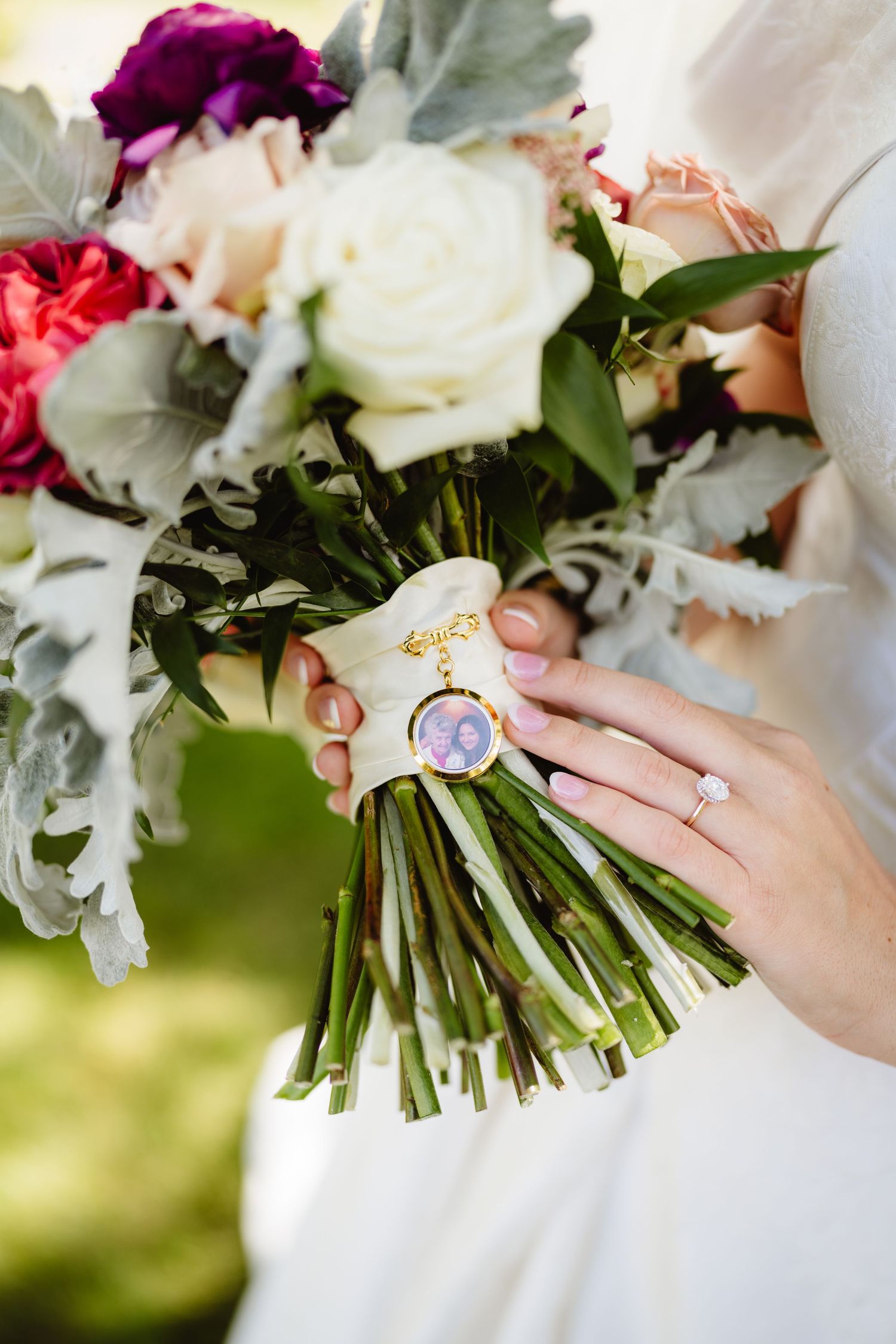 A bridal bouquet with white and burgundy roses features a sentimental photo charm attached to the stems.