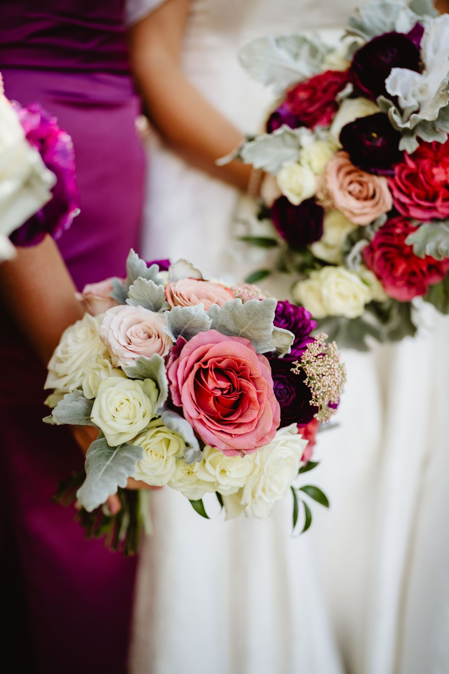 Elegant bridal bouquets featuring pink and white roses with purple accents line up beautifully against white fabric.