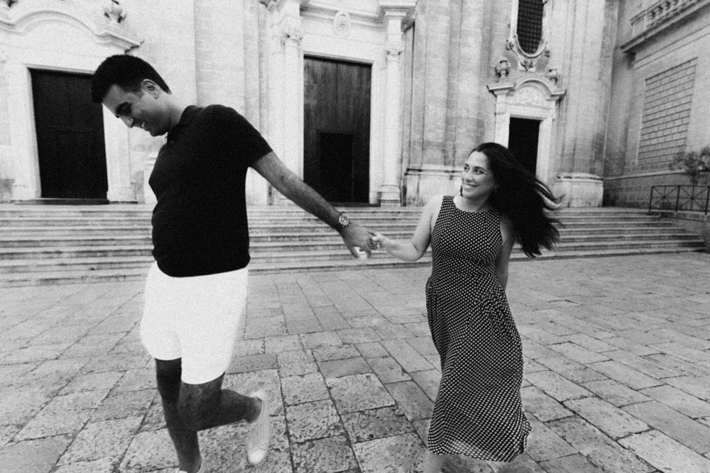 A black and white collage of dancers performing graceful movements on a cobblestone street in front of historic architecture.