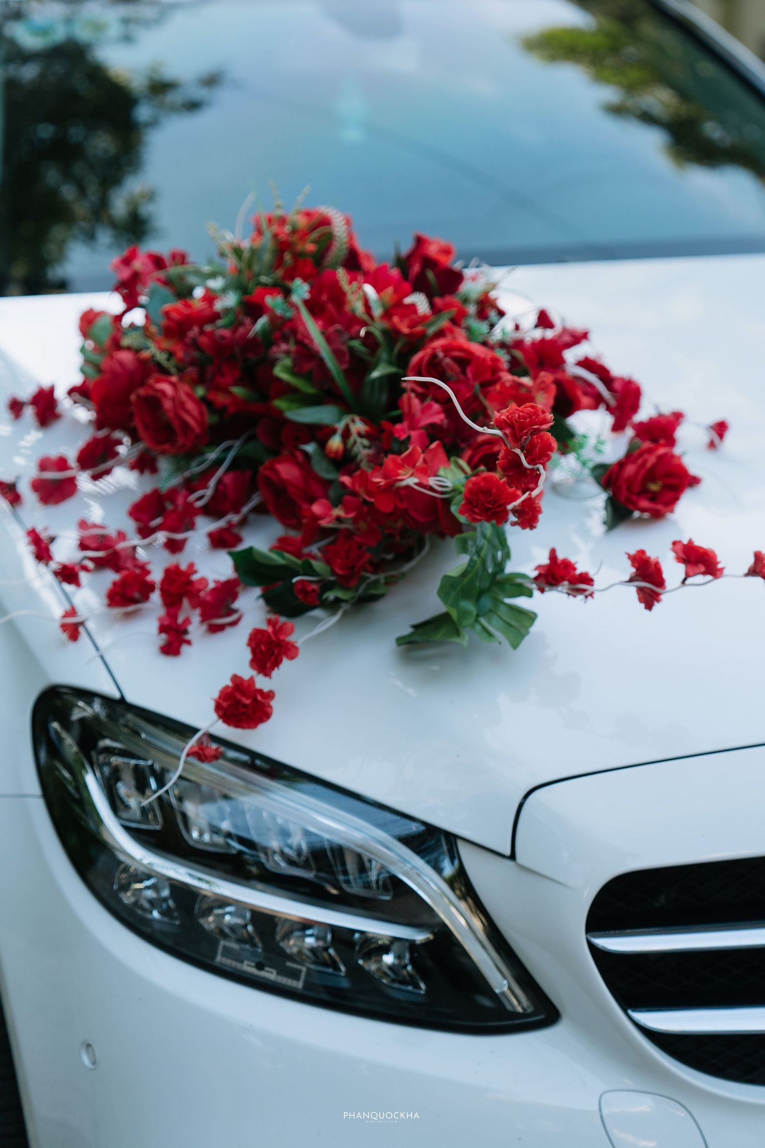 Red roses and carnations wedding car decoration on white Mercedes-Benz hood.
