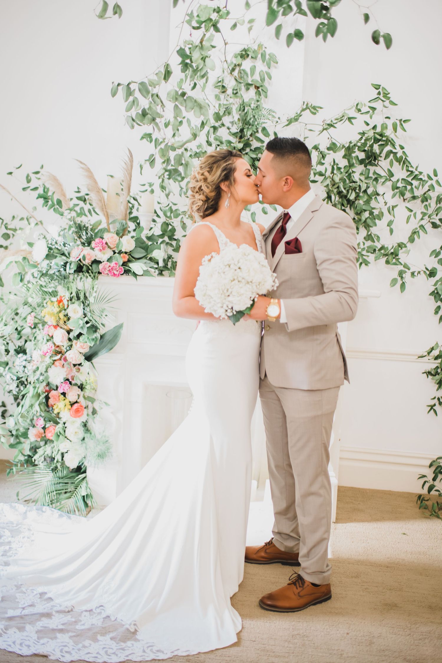 Bride and groom share a kiss at floral altar with white hydrangeas and greenery backdrop.