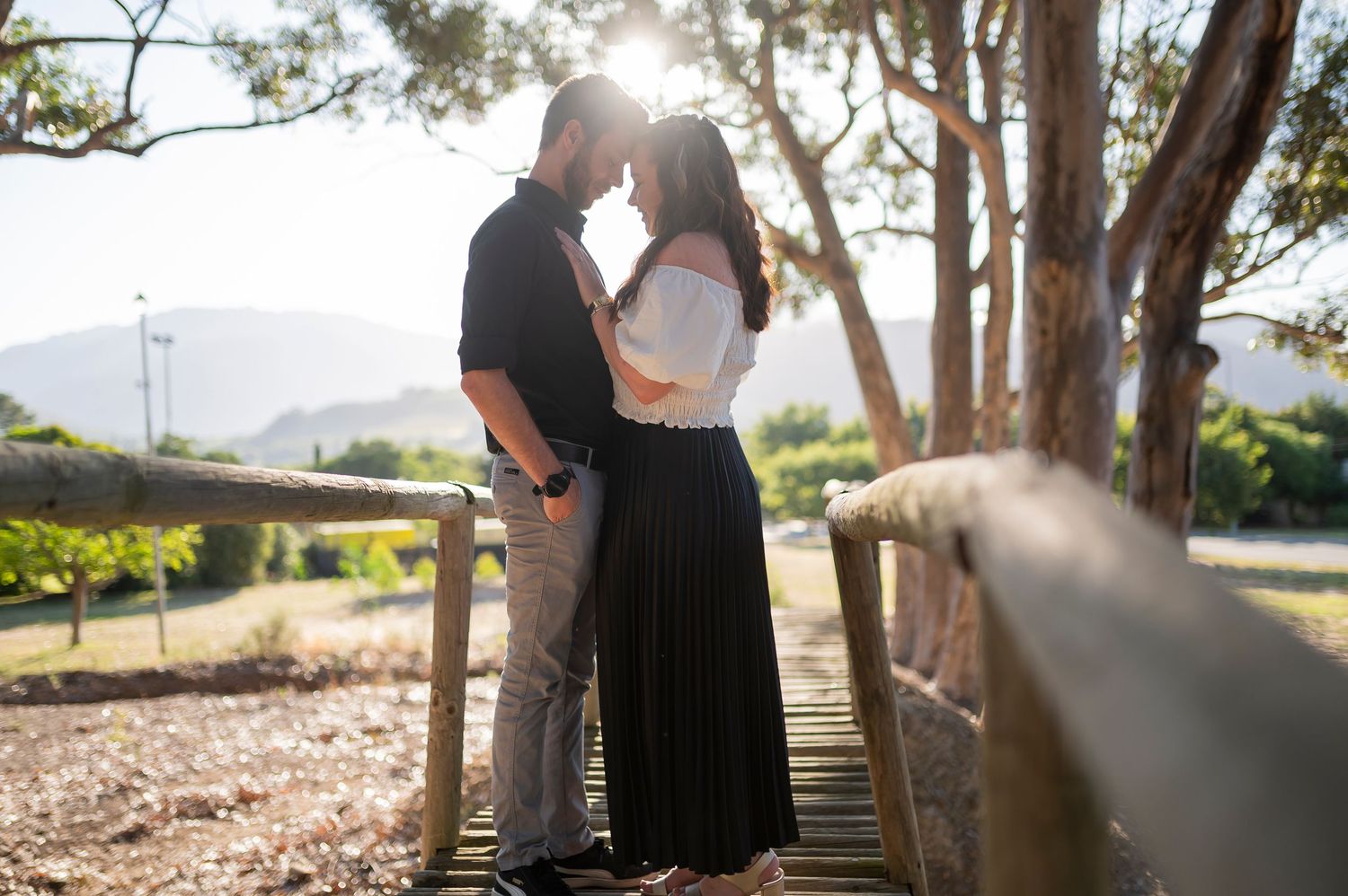 Romantic couple embraces in a sun-dappled forest setting with warm glowing backlight creating a dreamy atmosphere.