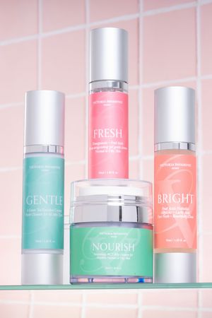 Pink pastel skincare products arranged on glass shelf with turquoise and coral colored packaging.
