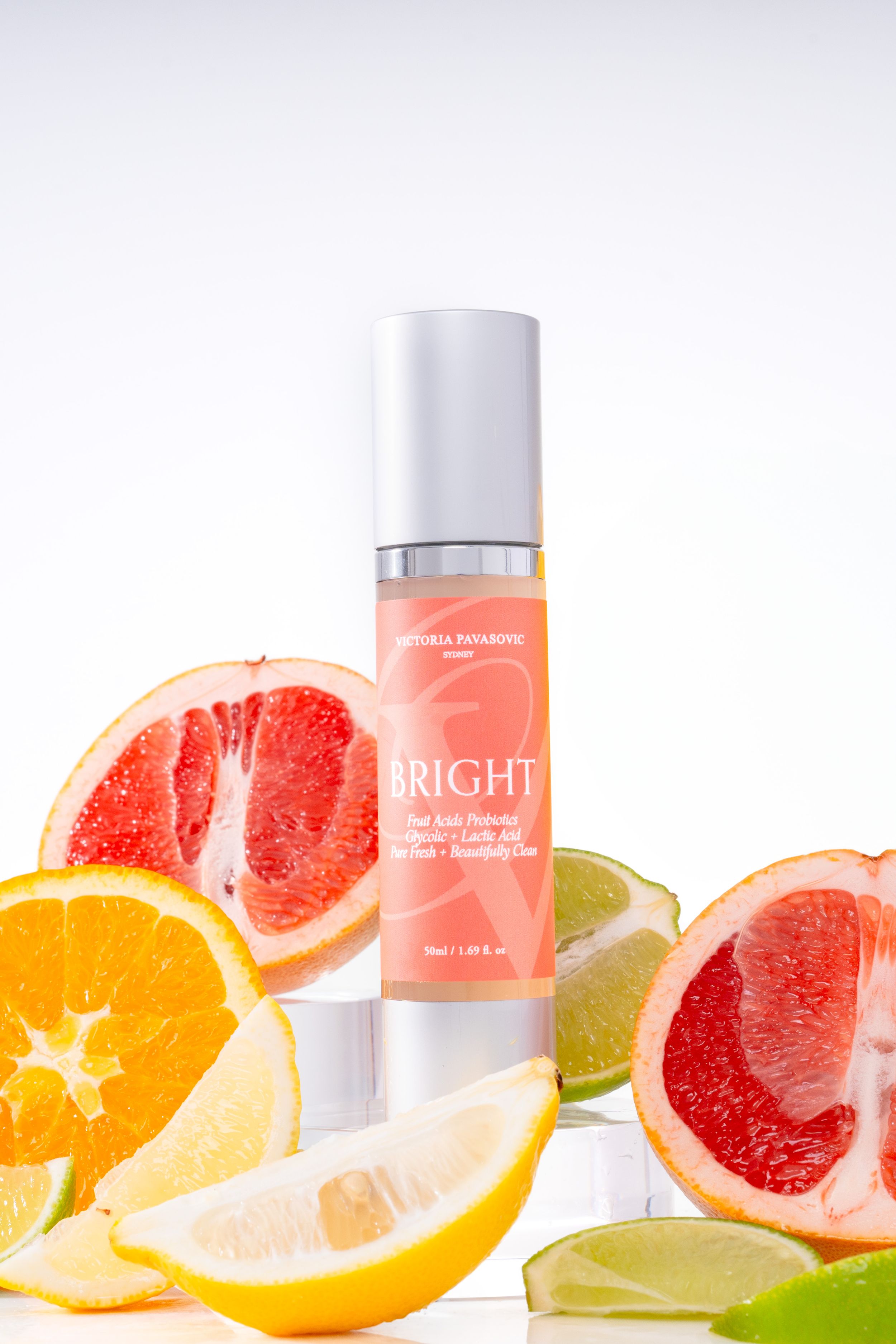 Fresh citrus fruits including grapefruit, orange and lime slices arranged with skincare product bottles on white background.