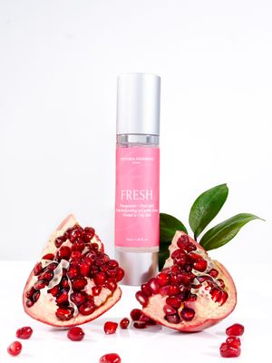 Fresh pomegranate slices and beauty products arranged on white surface with scattered red seeds.