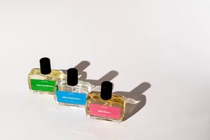 Colorful perfume bottles cast long shadows on white surface in minimalist composition.