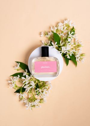Pink nail polish bottle surrounded by delicate white spring flowers and green leaves on a peachy background.