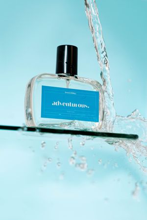 A blue perfume bottle floating in splashing crystal clear water against a turquoise background.