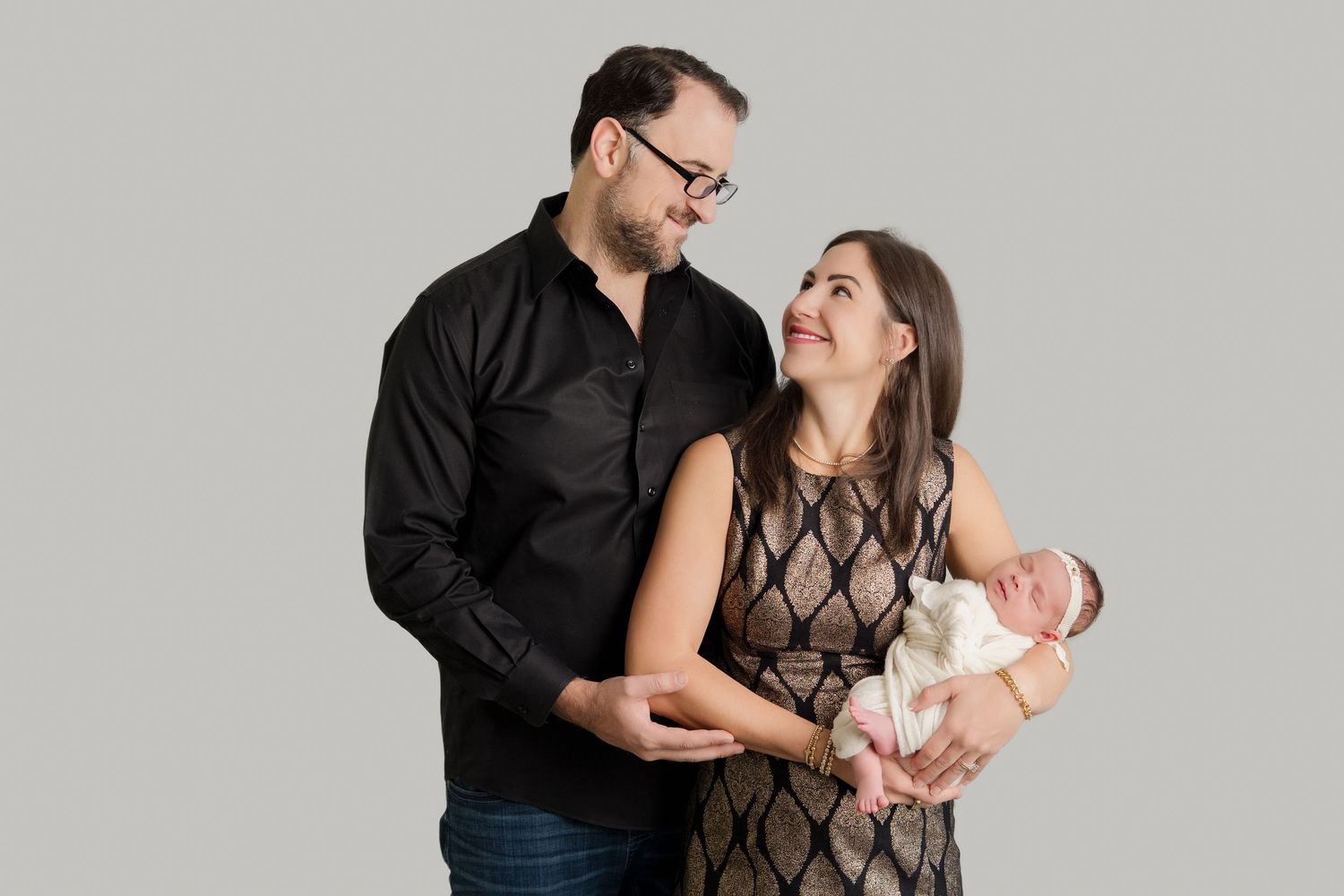 A family wearing black and brown outfits poses together in a professional studio setting against a grey background.