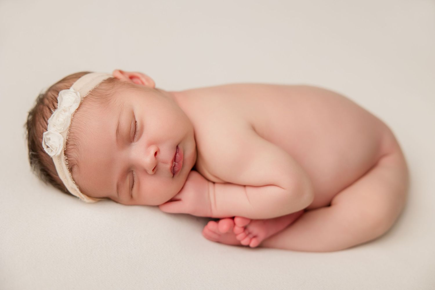 Peaceful newborn baby in white wrap sleeping soundly during professional portrait session.