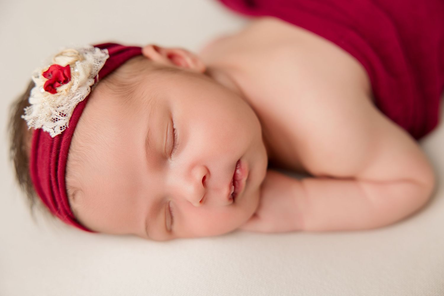 Sleeping newborn wearing a red headband with floral accent on white background.
