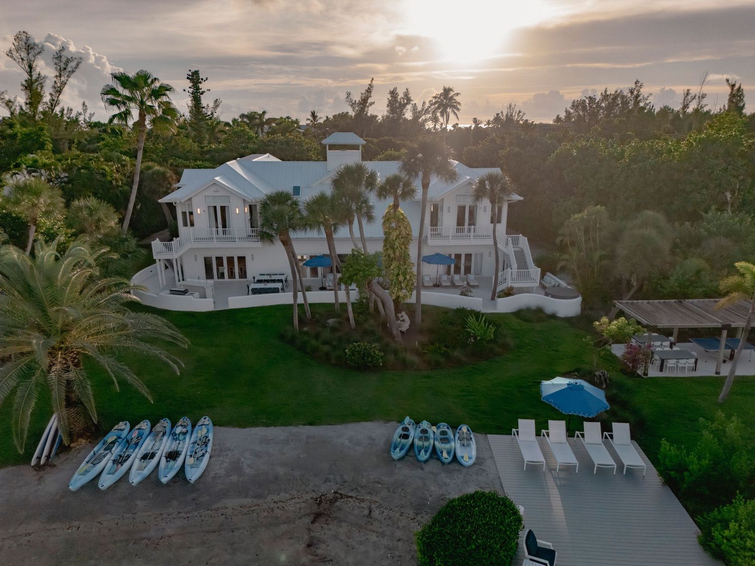 Aerial sunset view of waterfront property with kayaks and palm trees.