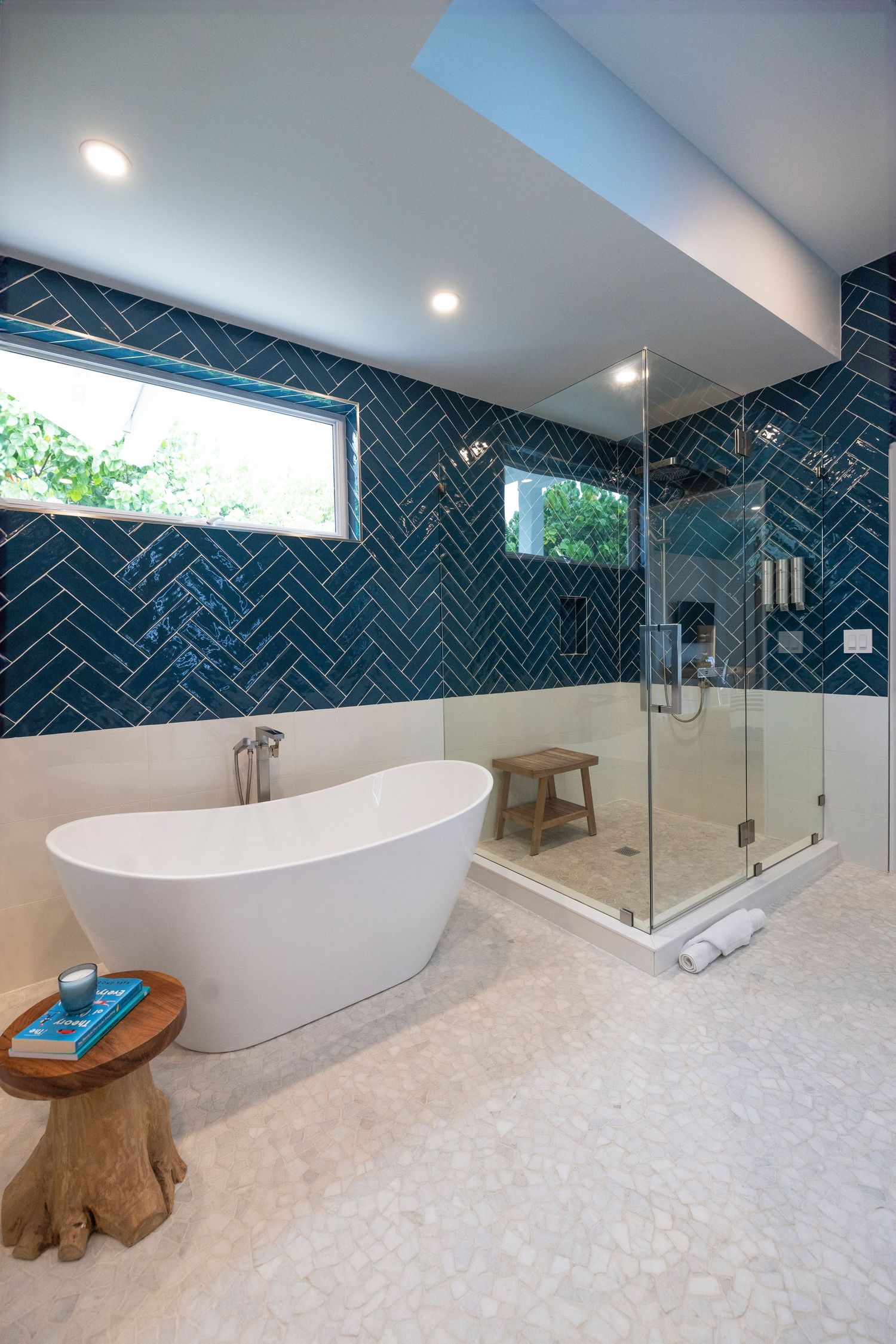 Modern bathroom with freestanding tub, teal herringbone tile walls, glass shower enclosure and natural wood accent stool.