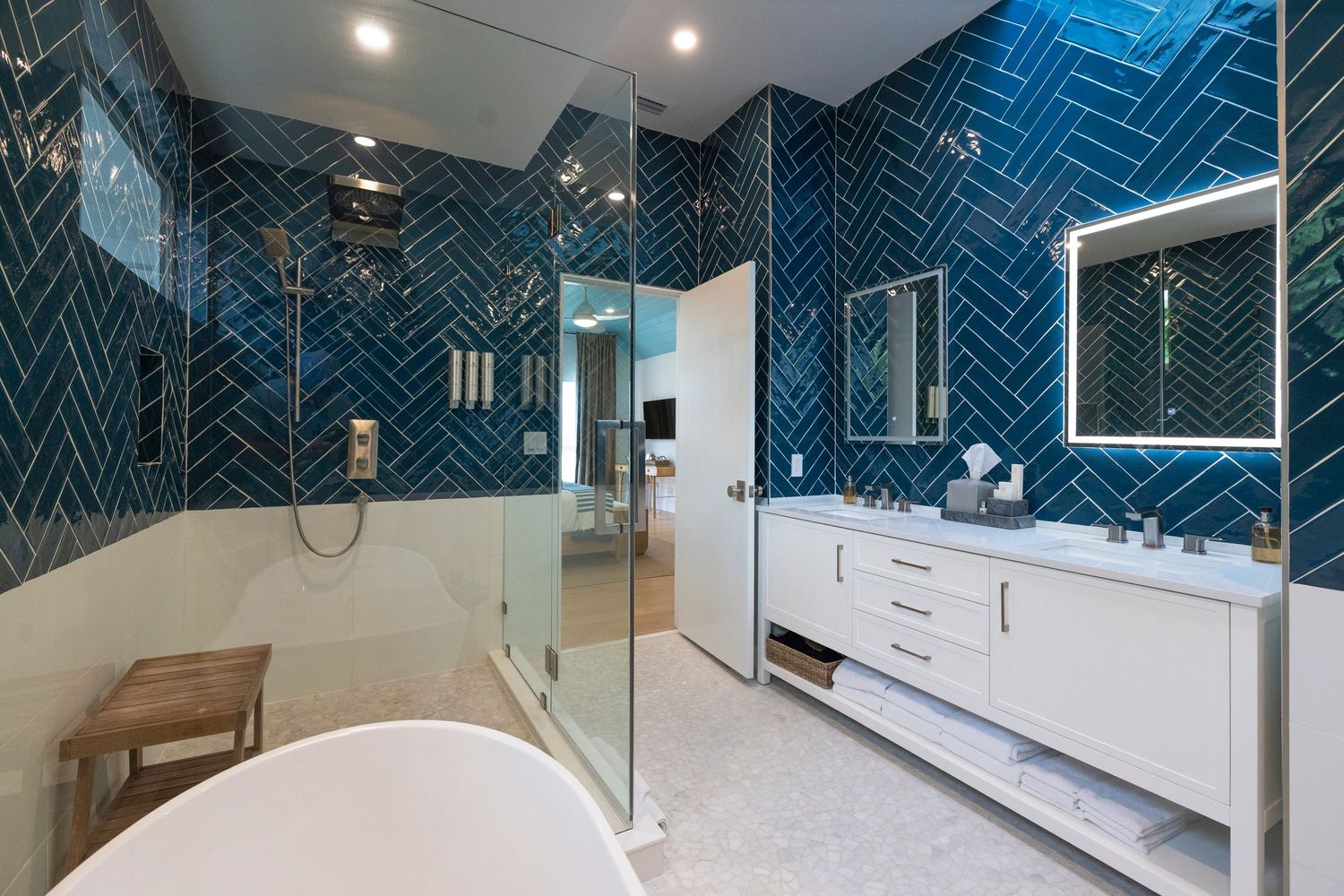 Modern bathroom interior featuring blue herringbone tile walls, glass shower enclosure, and bright lighting.