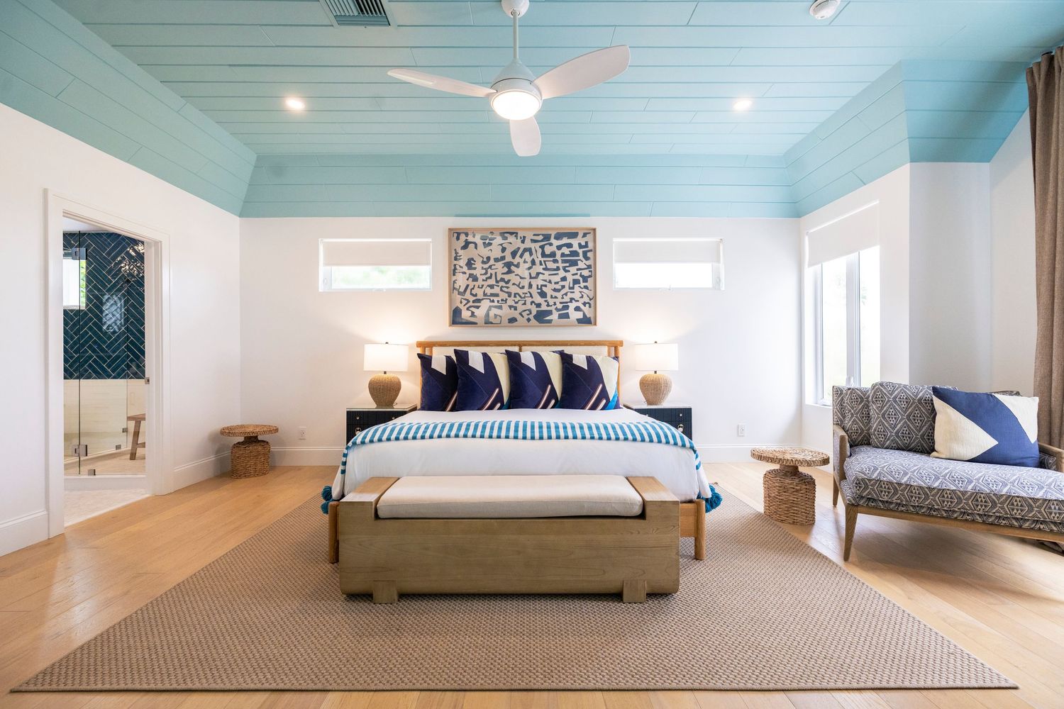 Modern bedroom interior with white walls, light blue ceiling, hardwood floors, and minimalist furnishings.