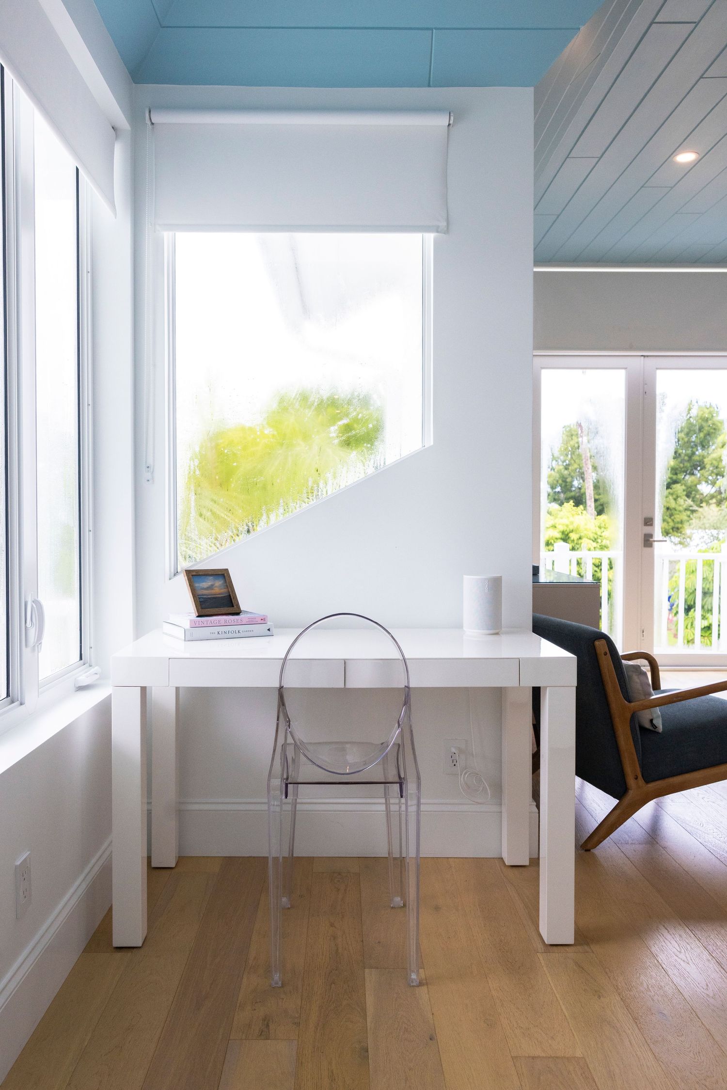 Bright modern room with white walls, hardwood floors, and a transparent chair near large windows letting in natural light.